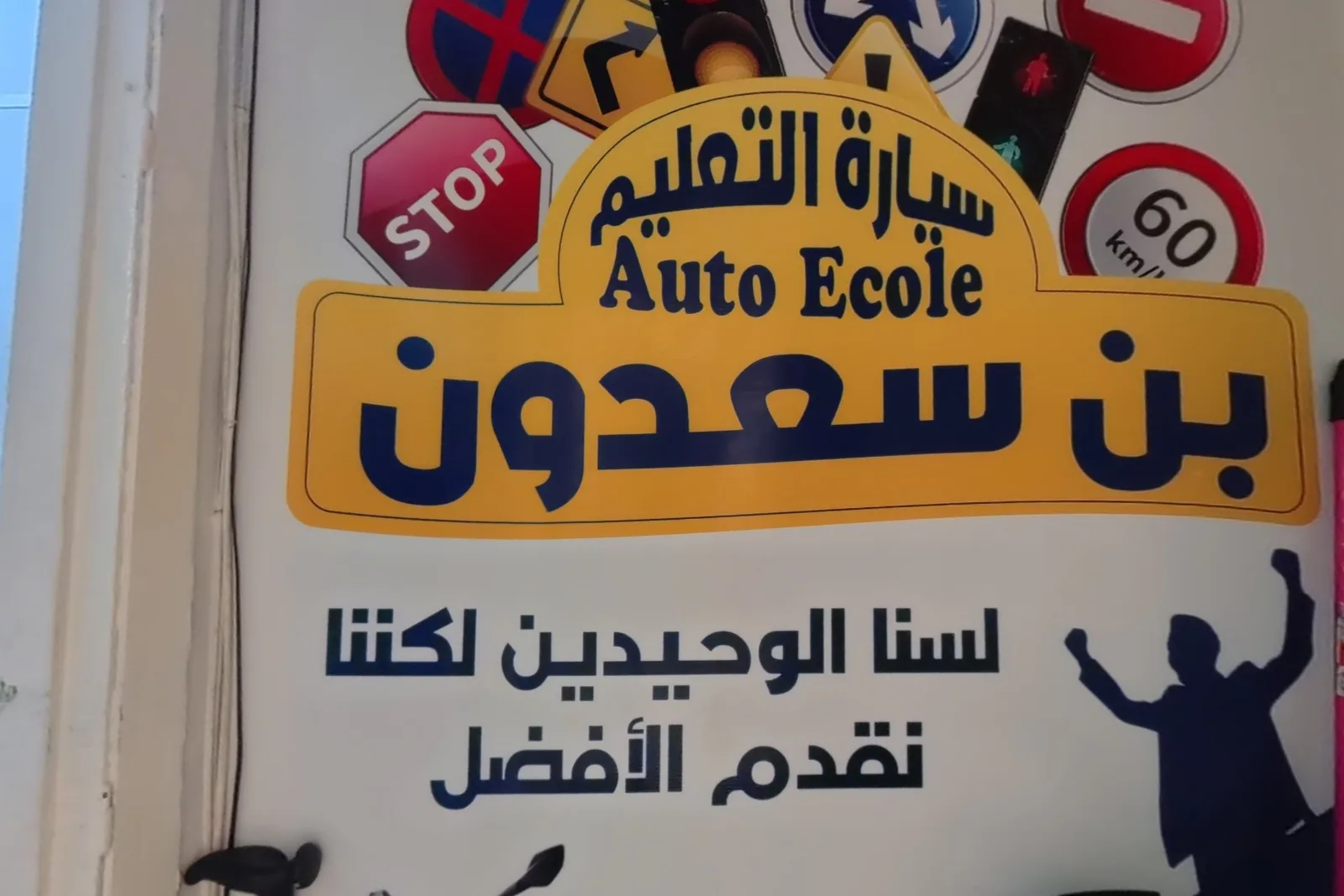 Mur de l’entrée de l’Auto-École Bensaadoun : logo jaune, panneaux et slogan « Nous ne sommes pas les seuls, mais nous offrons le meilleur »