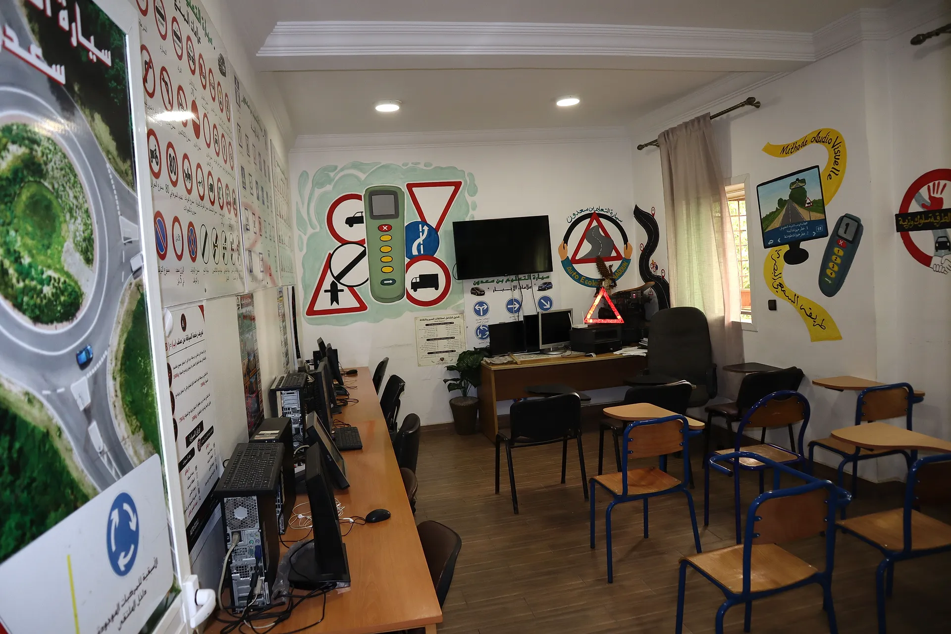 Salle de cours de l’auto-école : rangée d’ordinateurs pour le code, chaises-tablettes et fresques de panneaux